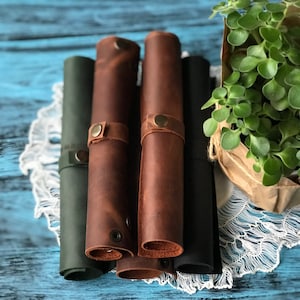 May include: Four rolled-up leather placemats in brown, green and black. The placemats are tied with leather straps and have decorative stitching.