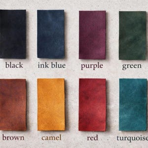 May include: Eight rectangular leather swatches arranged in two rows. Colors include black, ink blue, purple, green, brown, camel, red, and turquoise. Each swatch is labeled with its corresponding color name printed in a serif font below it.