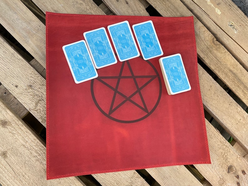 May include: Red leather tarot cloth with a pentagram design and five blue tarot cards placed around it.
