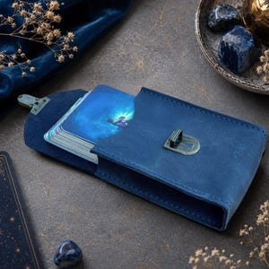 Könnte beinhalten: Ein blaues Kartenetui aus Leder mit Metallverschluss, das ein Kartenspiel mit blauen Himmelsmotiven enthält. Das Etui verfügt über einen Klappdeckel und eine rechteckige Struktur, die zum Aufbewahren und Schützen eines Kartenspiels dient.