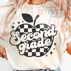 Puede incluir: Camiseta color crema con un diseño de manzana a cuadros en blanco y negro con las palabras "Second Grade" en una fuente lúdica. El diseño incluye acentos de estrellas y una hoja. La camiseta es de estilo casual.