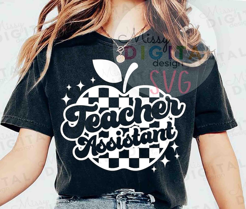 May include: Black t-shirt featuring a white and black checkered apple design with the words "Teacher Assistant" in a retro font. The design includes white star accents. A casual, comfortable top.