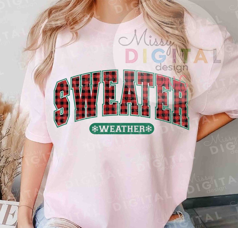 Puede incluir: Una camiseta rosa claro con las palabras "SWEATER WEATHER" en un dise&ntilde;o de cuadros rojos y negros. El texto est&aacute; delineado en verde. La camiseta es de cuello redondo.