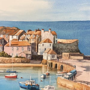 Op de afbeelding: Een aquarel schilderij van een klein havenstadje met kleurrijke huizen en boten. De lucht is blauw met witte wolken en het water is lichtblauw. Het schilderij is gesigneerd met "J.M. Kilburn".