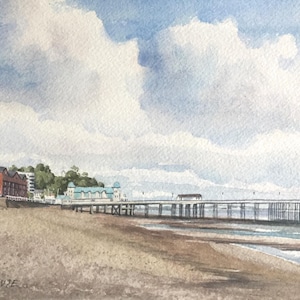 May include: A watercolor painting of a pier extending out into the ocean. The pier has a white wooden structure with a blue roof. There are buildings on the shore behind the pier. The sky is a light blue with white clouds.