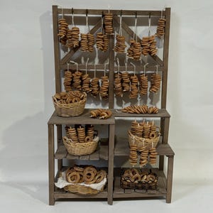 Op de afbeelding: Een houten stand met meerdere planken toont een verscheidenheid aan bruine, ringvormige gebakken producten. De stand heeft een rustieke, vintage uitstraling en is gevuld met manden met gebakken producten.