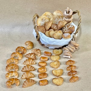 Op de afbeelding: Een rieten mand gevuld met verschillende gebakjes, waaronder croissants, broodjes en hartvormige gebakjes. De mand is omringd door een verzameling mini-croissants en hartvormige gebakjes.
