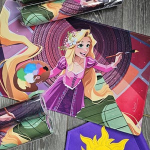 May include: Mouse pads featuring a cartoon illustration of a princess with long blonde hair, wearing a pink dress, holding a paintbrush and a palette of colors. Rolled-up mouse pads are also visible, along with a purple banner with a yellow sun.