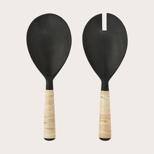 Op de afbeelding: Een set van twee zwarte serveerscheppen met natuurlijke geweven handvatten. De scheppen zijn ontworpen om salades te serveren.