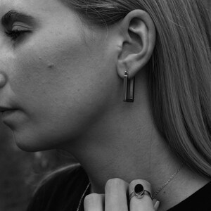 Peut inclure: Une femme portant une chemise noire et un collier en argent avec une bague ovale noire &agrave; son doigt. Elle porte une paire de boucles d'oreilles rectangulaires en argent.