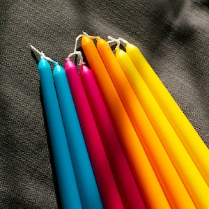 May include: A set of eight colorful candles, arranged in a rainbow pattern, with shades of blue, green, yellow, orange, red, and pink.
