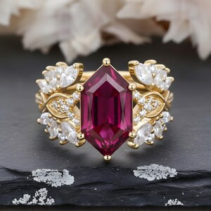 May include: A gold ring set with a large, faceted, deep red gemstone. The ring is surrounded by smaller white gemstones and intricate gold detailing, creating an elegant and luxurious design.