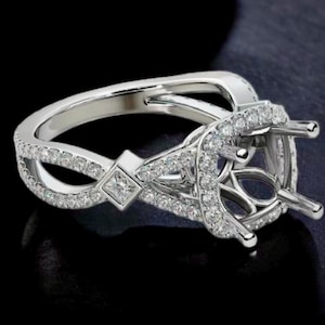 Könnte beinhalten: Eine silberne Ringfassung mit einem diamantförmigen Mittelstück und einer Pavé-Fassung aus kleineren Diamanten um das Band.