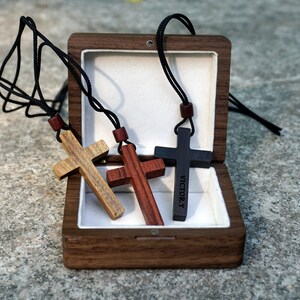 May include: Three wooden cross necklaces in a walnut wood box. The crosses are brown, red, and black. The black cross has the word "VICTORY" engraved on it.