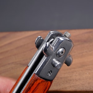 May include: Close-up of a pocket knife with a wood handle and a silver blade. The blade is partially open and the locking mechanism is visible.