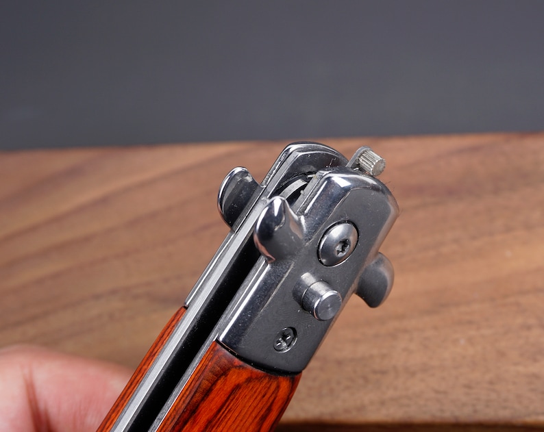 May include: Close-up of a pocket knife with a wood handle and a silver blade. The blade is partially open and the locking mechanism is visible.