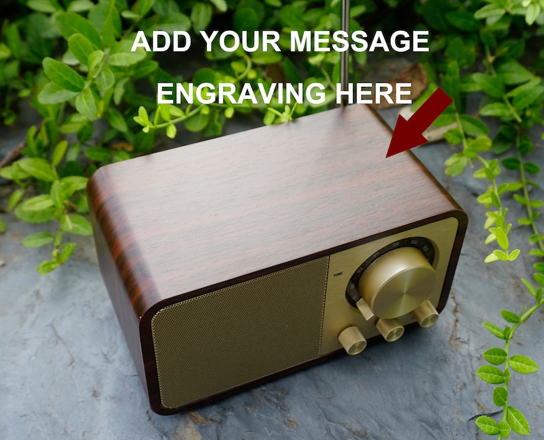 Pu&ograve; includere: Una radio in legno con una griglia per altoparlanti e manopole dorate. La parte superiore della radio &egrave; in legno e ha uno spazio per l'incisione. Il testo "ADD YOUR MESSAGE ENGRAVING HERE" &egrave; scritto sopra la radio.