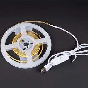 May include: A roll of yellow LED strip lights on a white spool, with a white USB cable and switch. The lights are designed for flexible use and are on a black background.