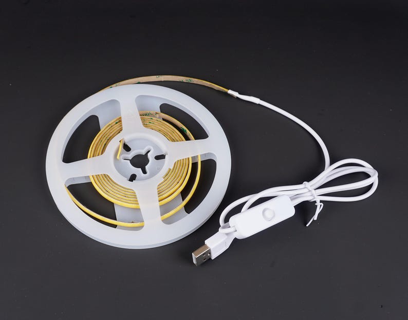 May include: A roll of yellow LED strip lights on a white spool, with a white USB cable and switch. The lights are designed for flexible use and are on a black background.