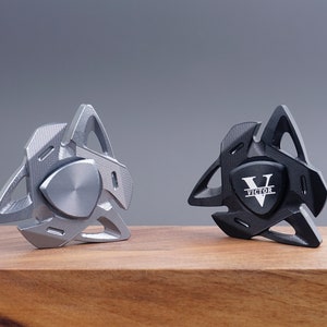 Puede incluir: Dos spinners de metal, uno plateado y otro negro. El spinner negro tiene el nombre "Victor" grabado.