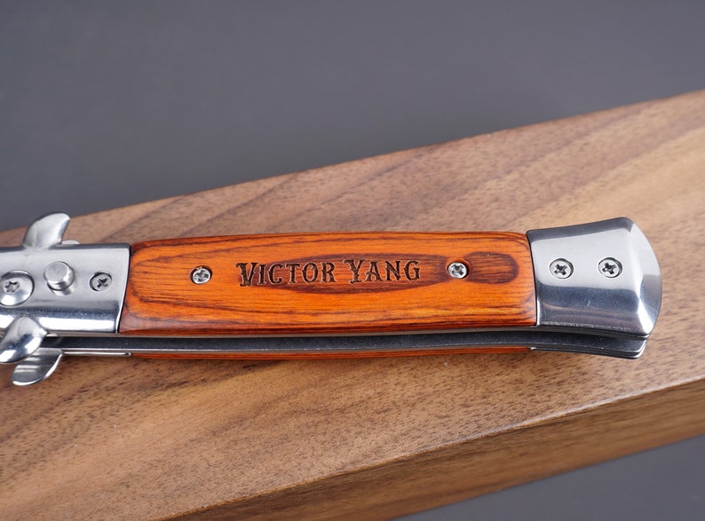 May include: A brown wooden handled pocket knife with a silver blade and the name "VICTOR YANG" engraved on the handle.