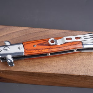 May include: A silver pocket knife with a wooden handle. The handle is a reddish brown color with a wood grain pattern. The knife has a silver clip on the back.