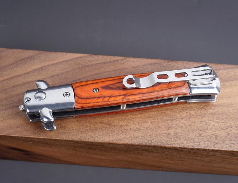 May include: A silver pocket knife with a wooden handle. The handle is a reddish brown color with a wood grain pattern. The knife has a silver clip on the back.