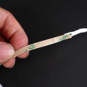May include: A close-up of a strip of brown tape with the text "300LSE" printed in green. The tape is adhered to a white cable. The background is black.