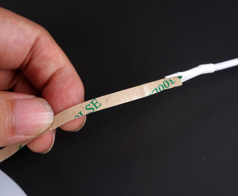 May include: A close-up of a strip of brown tape with the text "300LSE" printed in green. The tape is adhered to a white cable. The background is black.