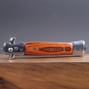 May include: A silver and wood pocket knife with the name "Victor Yang" engraved on the handle.