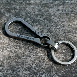 May include: A silver metal key chain with a large loop and a smaller ring. The key chain is engraved with the words "Arva Wong".