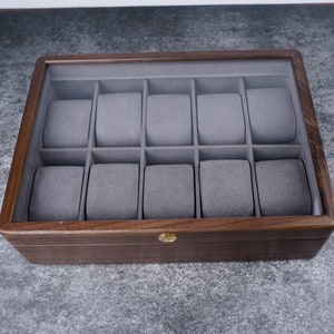 May include: A wooden watch box with a glass top and 12 individual compartments lined with gray felt.