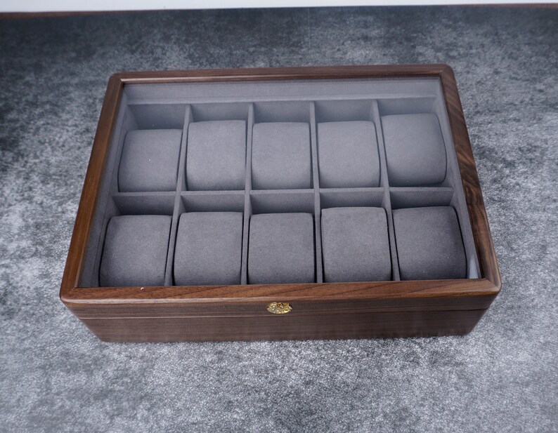 May include: A wooden watch box with a glass top and 12 individual compartments lined with gray felt.