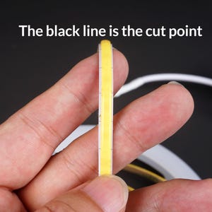 May include: A close-up of a flexible, yellow LED strip held between fingers. The text "The black line is the cut point" is visible at the top. The strip has a white border and is designed for cutting.