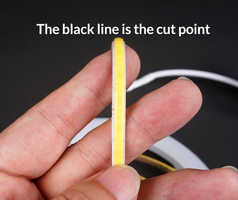 May include: A close-up of a flexible, yellow LED strip held between fingers. The text "The black line is the cut point" is visible at the top. The strip has a white border and is designed for cutting.