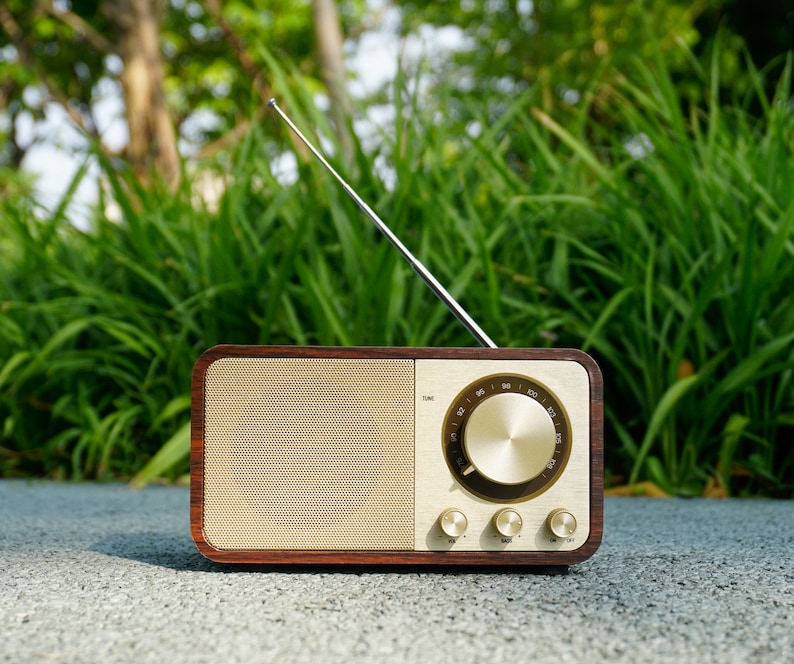 Pu&ograve; includere: Una radio in legno in stile vintage con un quadrante dorato e un'antenna argentata. La radio ha una cassa in legno marrone e una griglia dell'altoparlante beige.