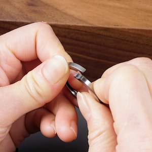 Può includere: Una persona tiene in mano un anello di metallo argentato con un'apertura. L'anello viene aperto.