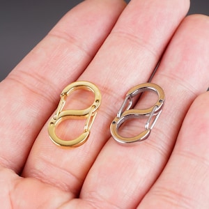 May include: Two double-ended keychains, one gold and one silver, are shown in a hand. The keychains are made of metal and have a simple design.