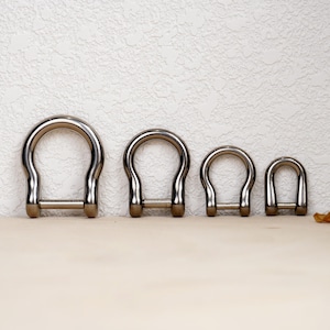 May include: Four silver metal D-rings of different sizes. The rings are arranged in order of size, with the largest ring on the left and the smallest ring on the right.