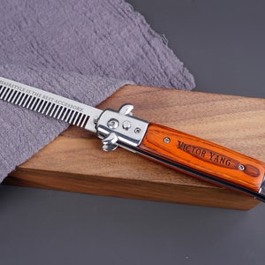 May include: A silver comb with a wooden handle engraved with "Victor Yang" and the text "A great hairstyle is the best accessory." The comb is lying on a wooden surface.