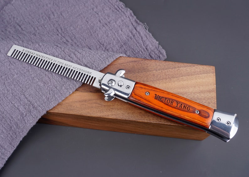 May include: A silver comb with a wooden handle engraved with "Victor Yang" and the text "A great hairstyle is the best accessory." The comb is lying on a wooden surface.