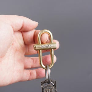 May include: A brass key chain with a D-shaped ring and a small, rectangular tag that says "NOMAD".