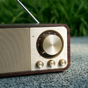 Pu&ograve; includere: Una radio in legno in stile vintage con un quadrante e manopole dorate. La radio ha una griglia dell'altoparlante con un motivo a maglia fine. Il quadrante ha numeri da 92 a 100 e le parole "TUNE", "BASS" e "VOL".
