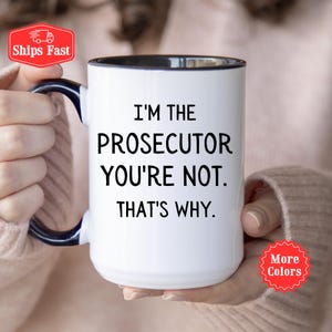 May include: White ceramic coffee mug with a black rim and handle. The mug has black text that reads "I'm the Prosecutor You're Not. That's Why."