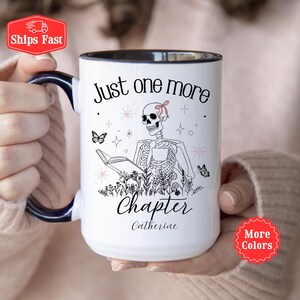 Puede incluir: Taza de cerámica blanca con interior y asa negros. La taza presenta un esqueleto leyendo un libro, con el texto "Just one more chapter" y el nombre "Catherine". También se incluyen mariposas y elementos florales.