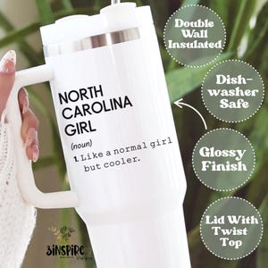 May include: White insulated tumbler with a handle, featuring the text "NORTH CAROLINA GIRL" and a definition. Additional text indicates it is double-wall insulated, dishwasher safe, has a glossy finish, and a lid with a twist top.