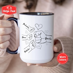 Puede incluir: Taza de cerámica blanca con interior y asa negros. La taza presenta un dibujo lineal negro de puños chocando, con los nombres "Nicholas", "Nina", "Natalie" y "Uncle" escritos en ella, junto con formas de corazón.