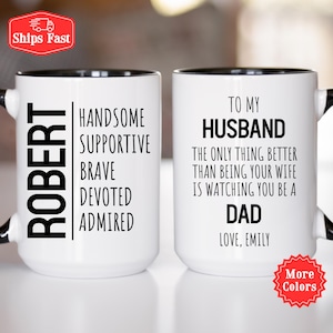 May include: Two white ceramic mugs with black rims and handles. One mug has the name "ROBERT" vertically, with the words "Handsome, Supportive, Brave, Devoted, Admired." The other mug says "To My Husband" and "The only thing better than being your wife is watching you be a Dad."