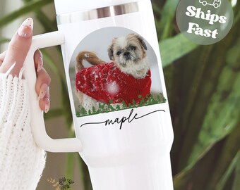 May include: White travel mug featuring a photo of a Shih Tzu wearing a red sweater. The dog is set against a snowy background with a green forest border. The name "maple" is written in cursive below the image.