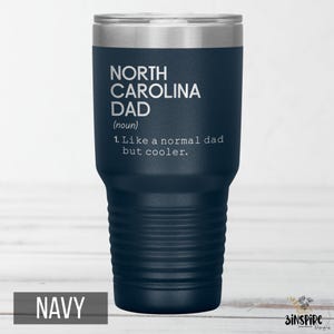 May include: Navy blue insulated tumbler with a silver lid. The tumbler features the text "NORTH CAROLINA DAD (noun) 1. Like a normal dad but cooler." The word "NAVY" is at the bottom of the tumbler.